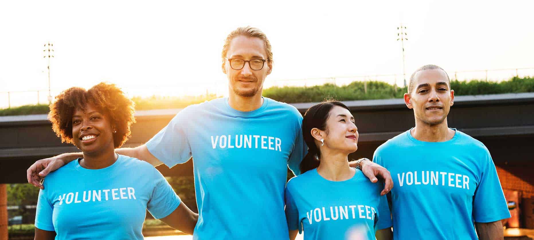 Not-for-profit: Four people with arms on shoulders wearing t-shirts with the word "volunteer"