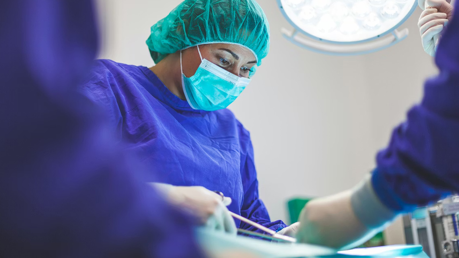 A medical professional wearing a surgical mask, cap, and gown performs a procedure in an operating theatre under bright lights, demonstrating precision and real-time insight essential for patient care.