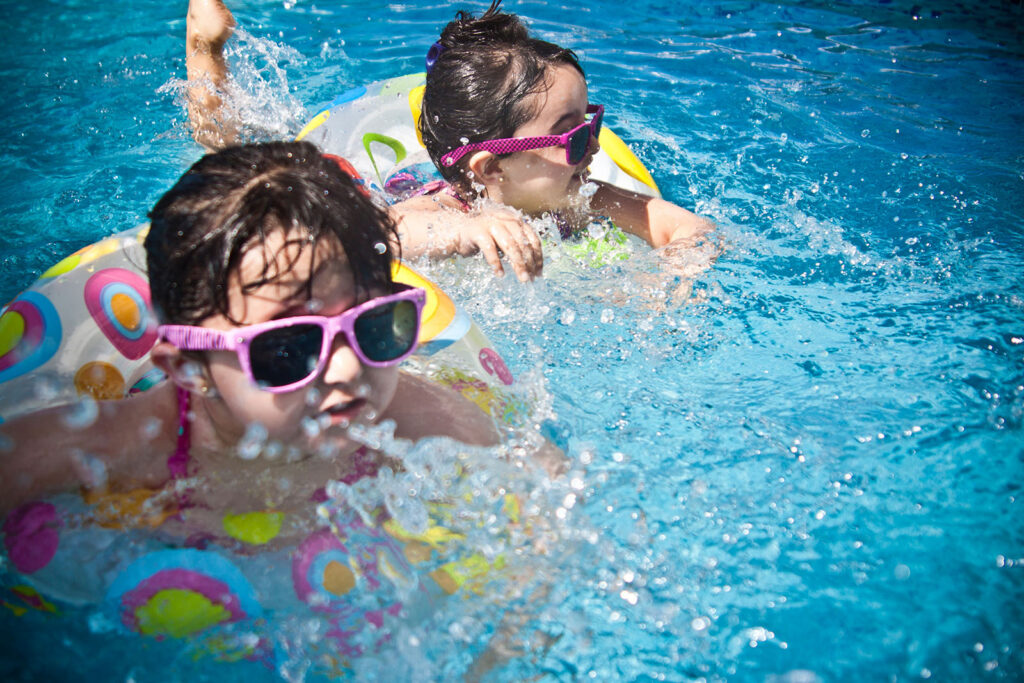 Two children wearing sunglasses swimming in pool water