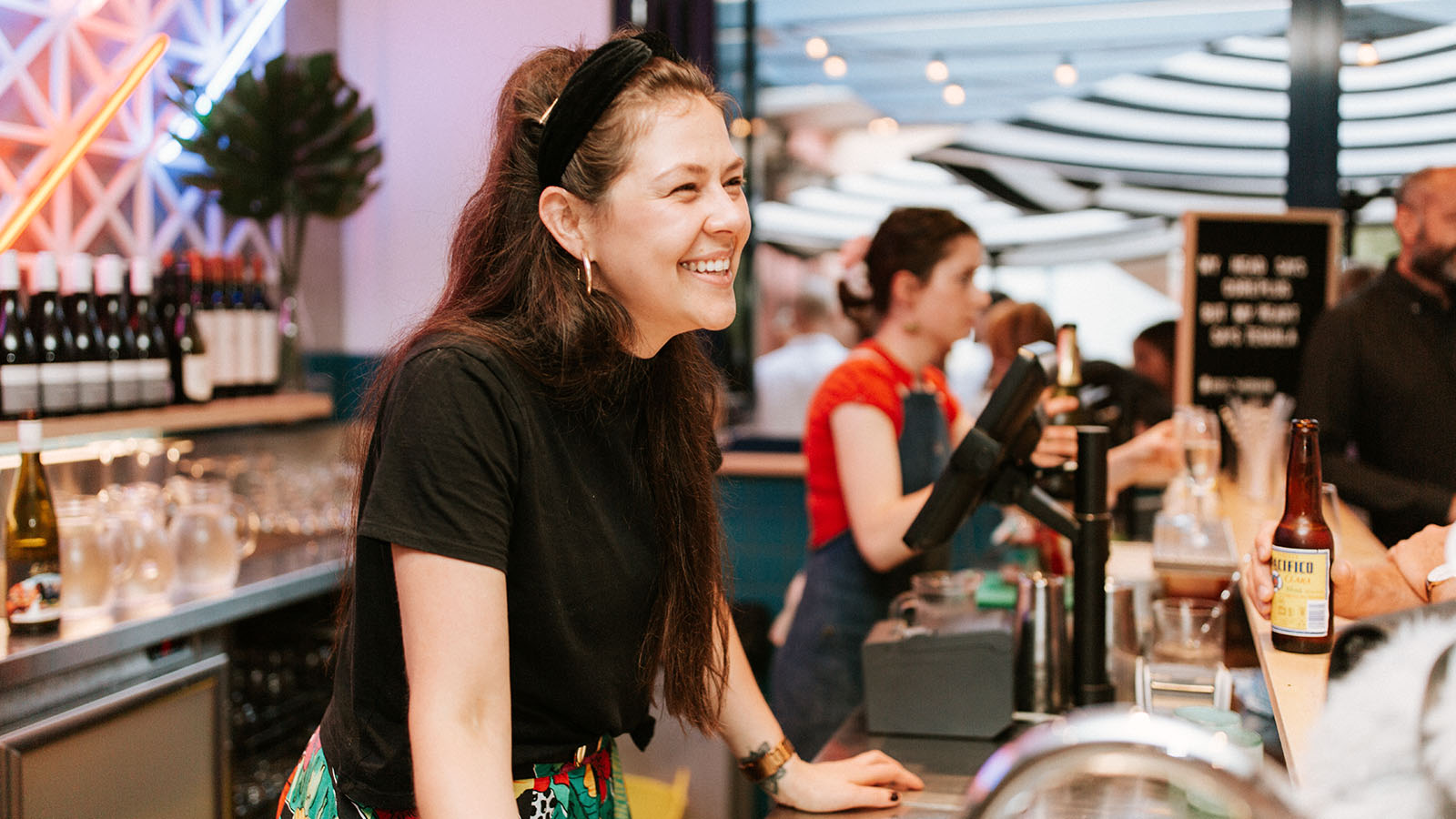 A woman in a black shirt smiles whilst standing behind a Fonda bar counter