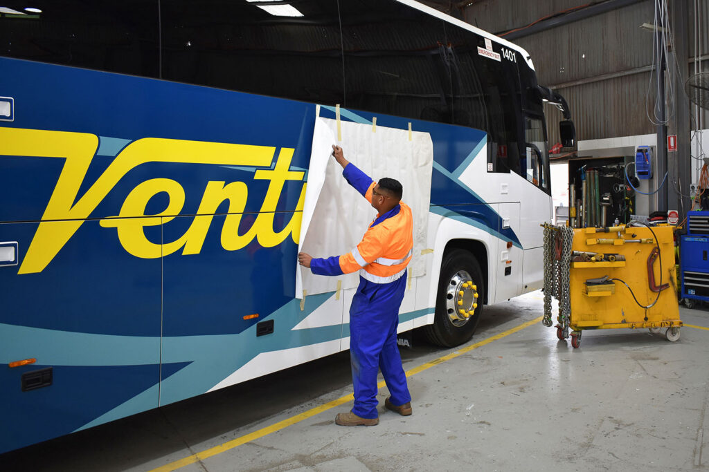 A worker in a high-visibility uniform working on a Ventura bus