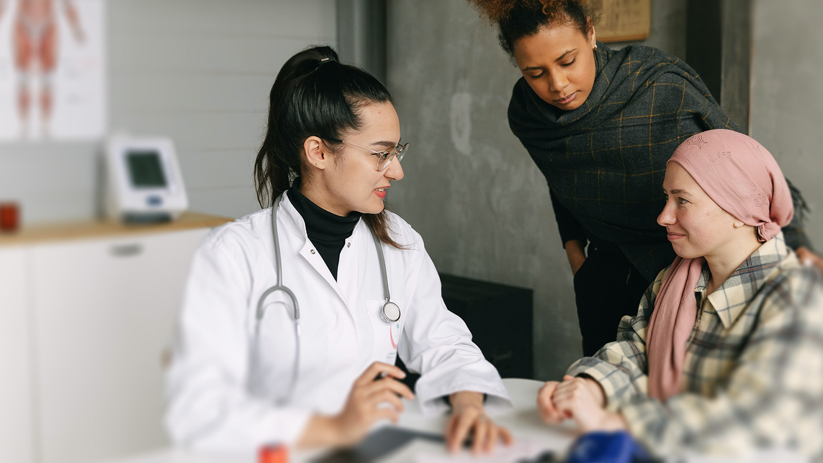 A doctor discusses healthy planning with a patient wearing a headscarf, whilst another person stands beside them in the medical surgery.