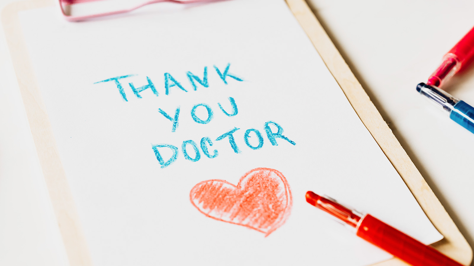 A handwritten note on a clipboard reads "Thank you doctor" in blue crayon with a red heart drawn below