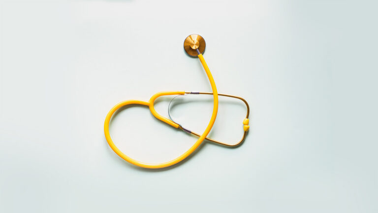 A yellow stethoscope with brass accents is laid out on a light background