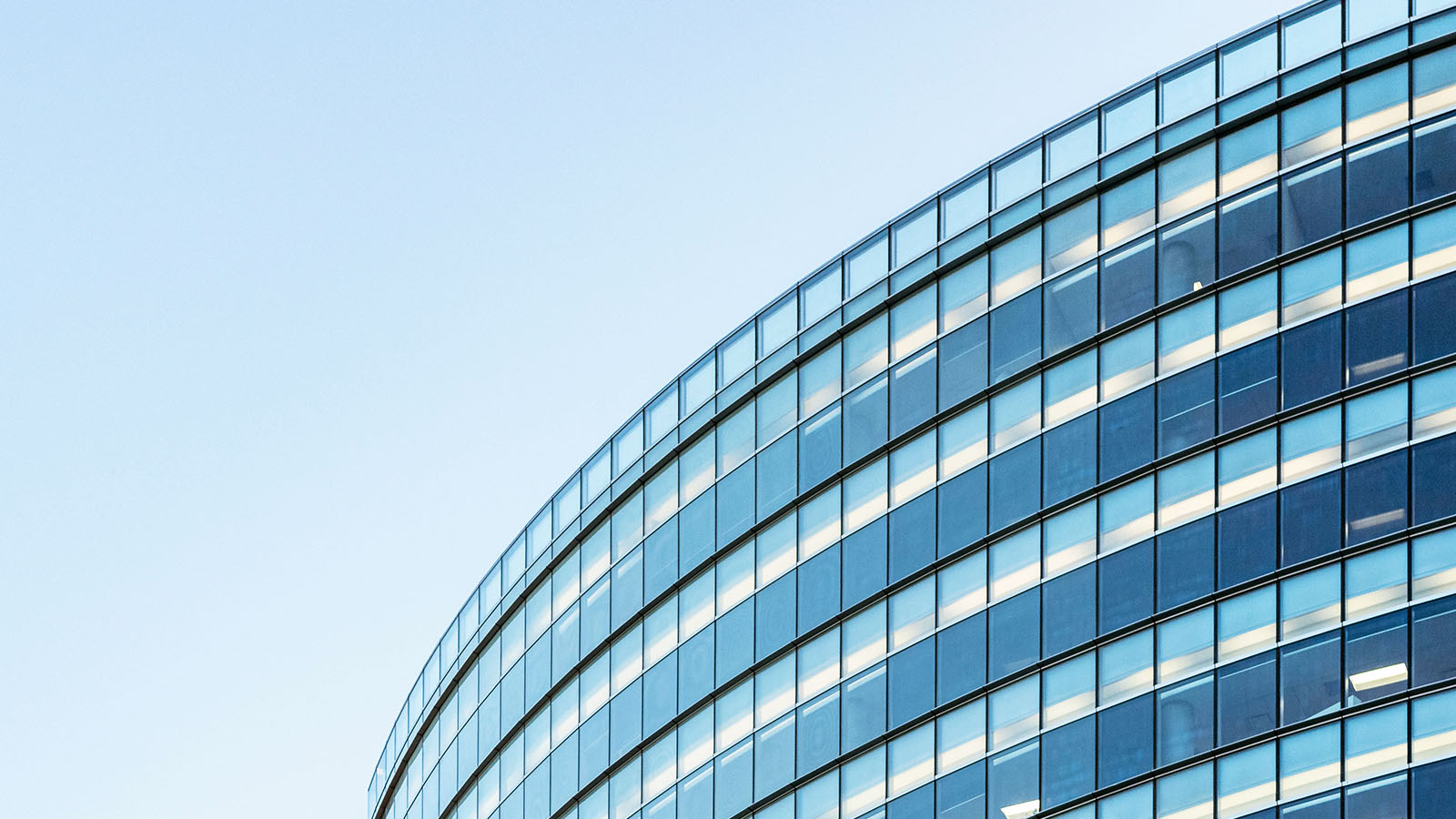 Curved glass office building with multiple floors and rows of windows under a clear blue sky