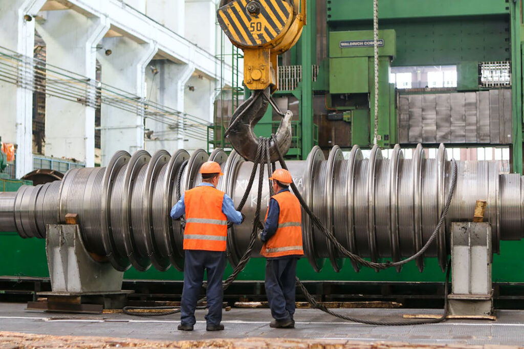 Two workers in safety vests next to a large industrial machine