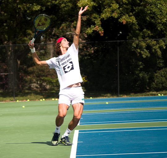 Man at tennis court, reaching high to hit a tennis ball