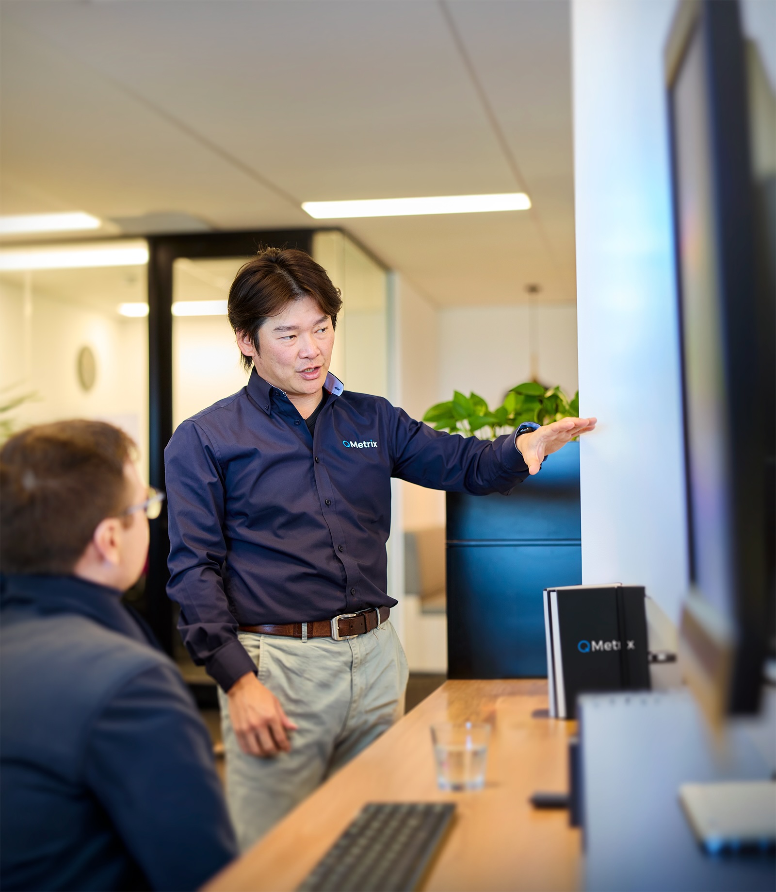 A person standing and gesturing, talking to another person sitting
