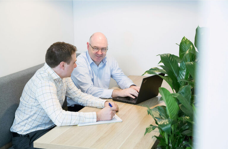 Two men sit at table with laptop