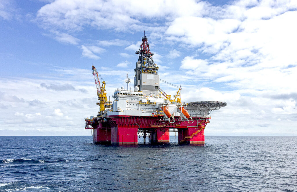 A large offshore oil drilling platform with red supports is stationed in open water