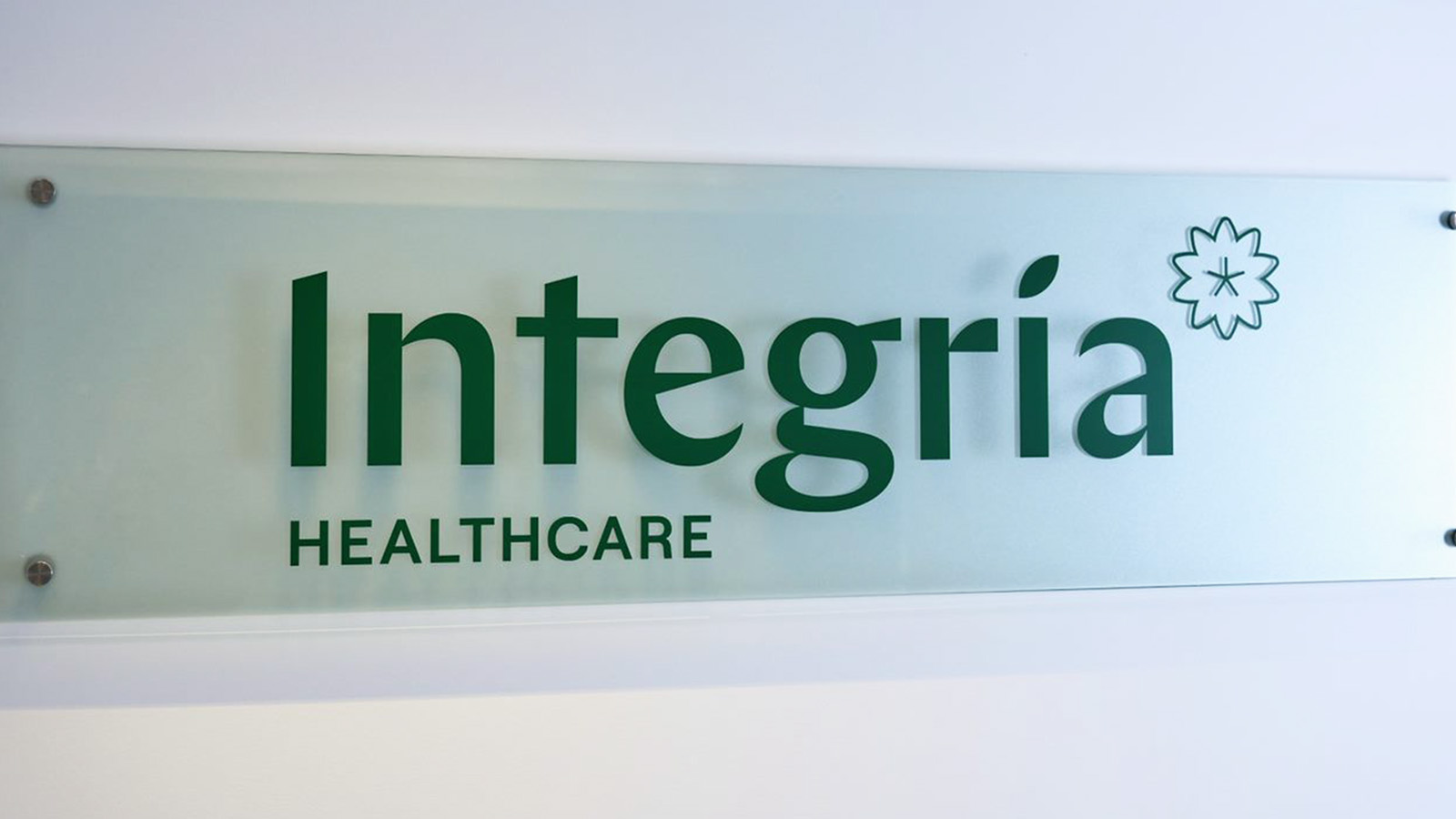 A frosted glass sign displays the text "Integria Healthcare" with a flower-like logo above the final "a," reflecting the company's focus on planning and innovation.