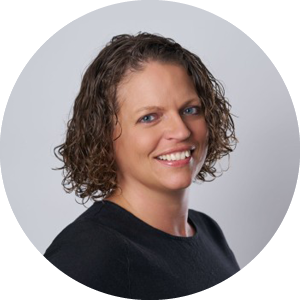 A woman with short, curly brown hair wearing a black top, smiling and facing slightly to the right in front of a plain light background—reflecting the confidence that comes from better planning at Integria Healthcare.