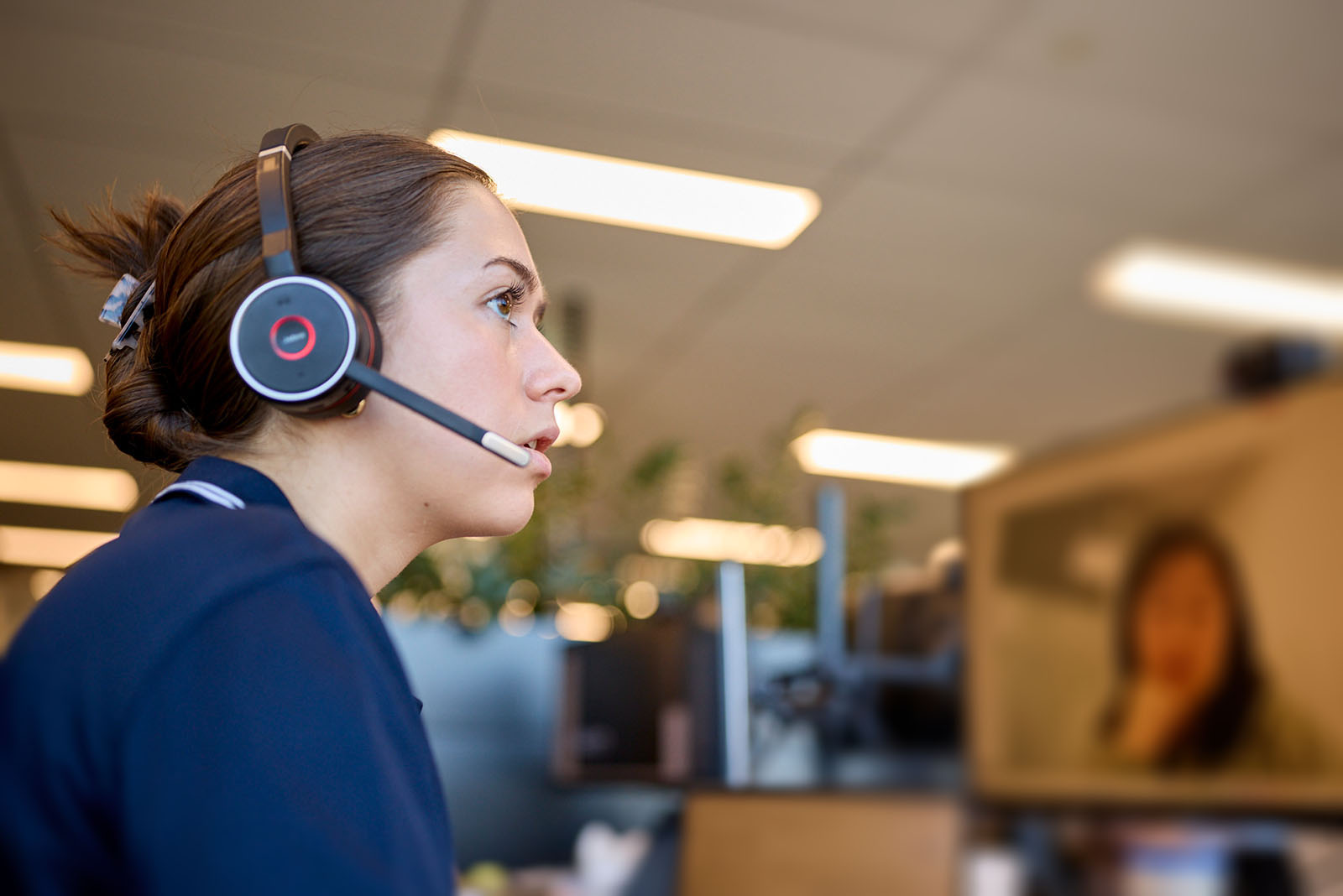 Woman wearing a headset sits at a desk, looking at a computer screen