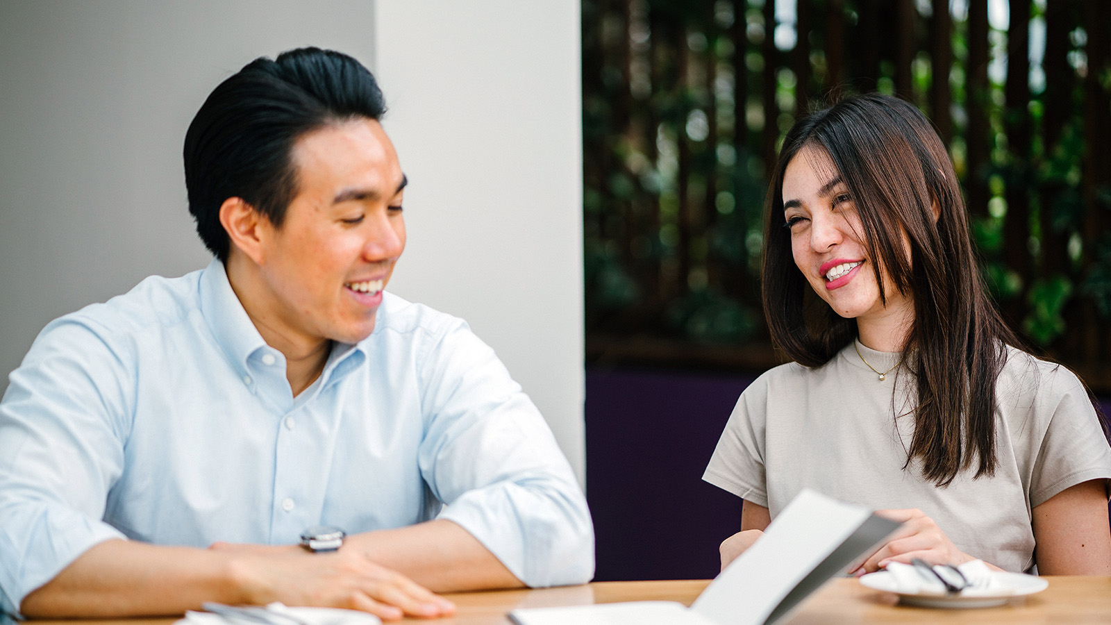Two people sit at a table, smiling and talking