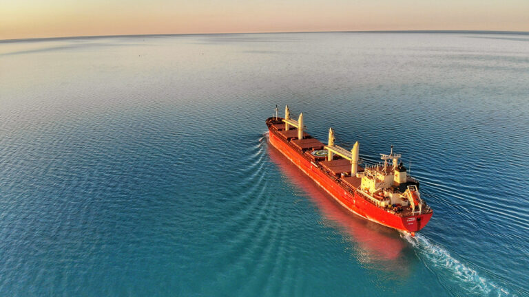 A large cargo ship sails across calm, blue water