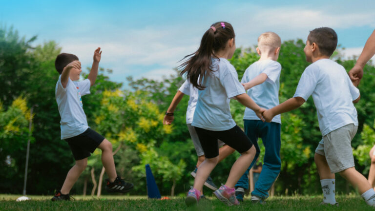 Children run and play together on a grassy field with trees in the background