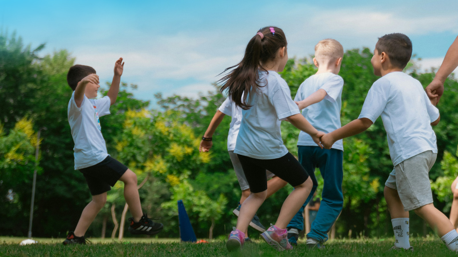 Children run and play together on a grassy field with trees in the background