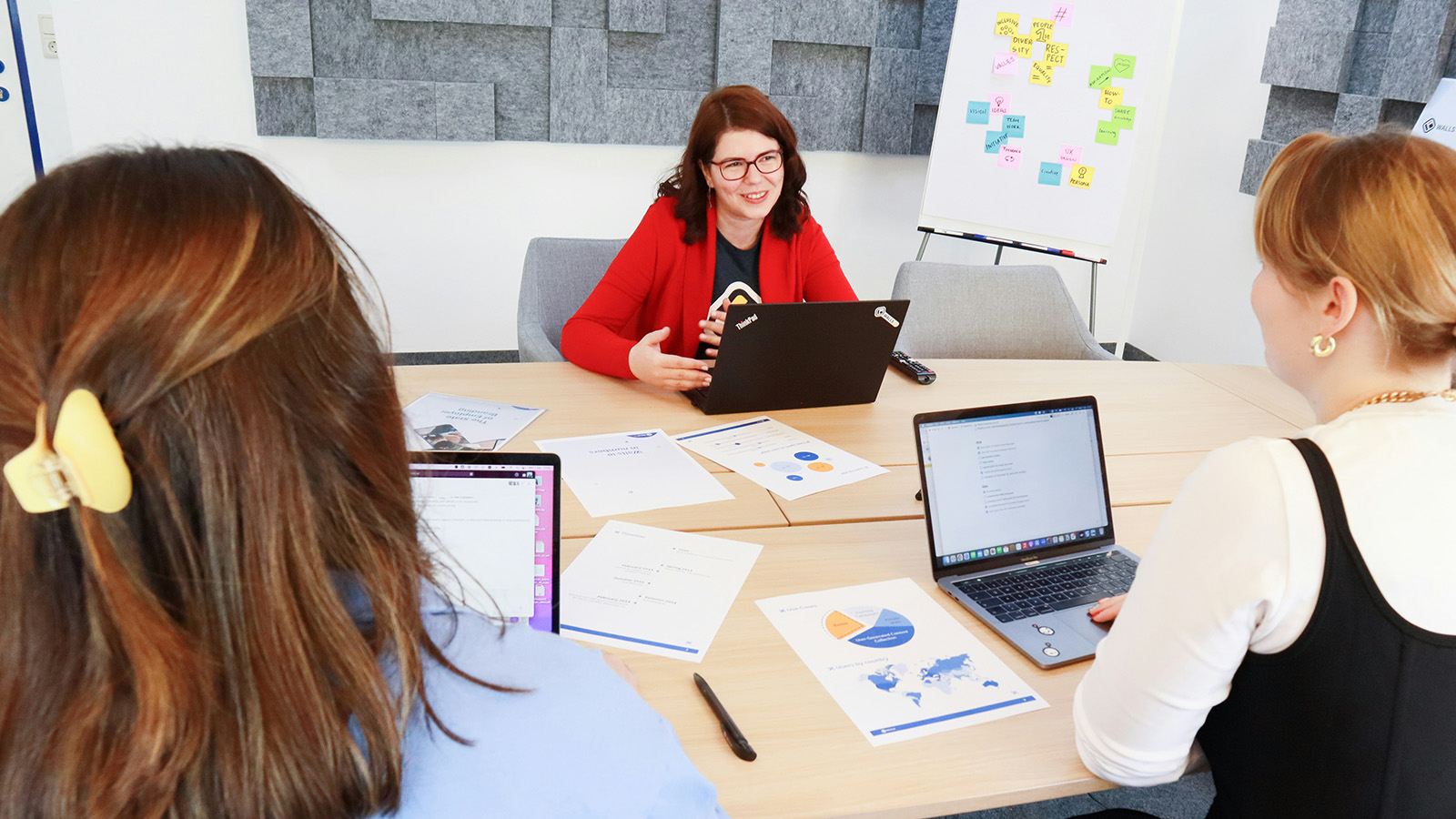 Three women sit at a table with laptops